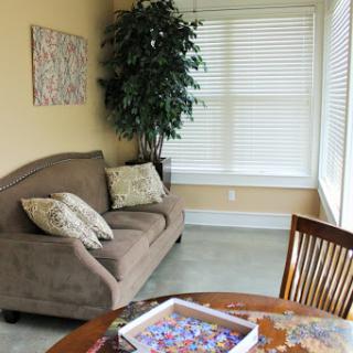 A cozy living area featuring a comfortable sofa, a dining table with a puzzle in progress, and natural light streaming through the window.