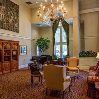 A spacious and elegant living room featuring classic furniture, a grand piano, a large chandelier, and a cozy seating area with bookshelves.