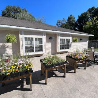 A bright and sunny day featuring a well-maintained garden with flower beds in front of a cozy house.