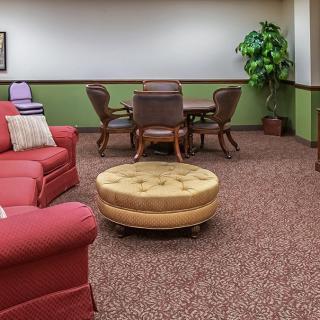 A cozy living room area with a red sofa, round ottoman, chairs around a table, and a potted plant.