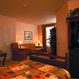 A cozy bedroom with warm lighting, featuring a bed, armchairs, and decorative elements.