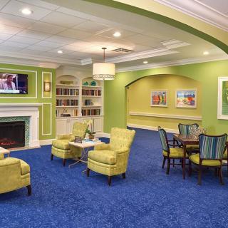 A cozy living room with green walls, blue carpet, and a comfortable seating area around a fireplace.