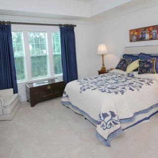A cozy bedroom with blue and white decor, featuring a neatly made bed, a window with blue curtains, and a bedside lamp.