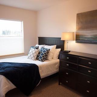 A cozy and well-decorated bedroom featuring a bed with pillows, a lamp on the nightstand, and modern artwork on the wall.