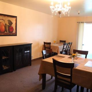 A cozy dining room with two tables, chairs, a chandelier, and a wall painting.