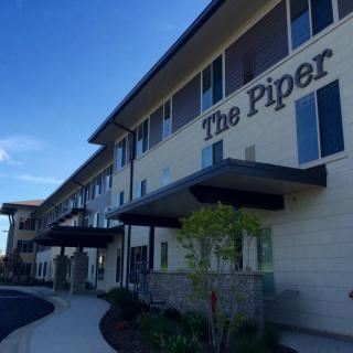 A modern building with the name 'The Piper' on its facade, set against a clear blue sky.