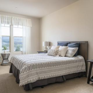 A minimalist bedroom with ample natural light, featuring a neatly made bed and decorative pillows.