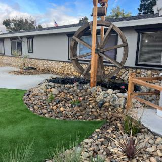 A beautifully designed outdoor landscape featuring a decorative wheel, rocks, and artificial grass.