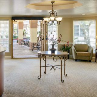 A cozy lobby area featuring a central table with a chandelier overhead, armchair seating, and large windows providing natural light.