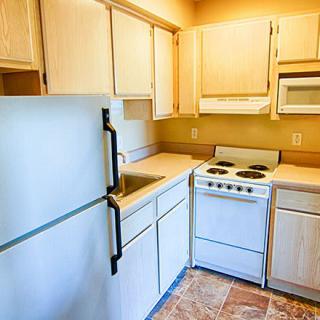 A compact kitchen with light-colored cabinets, a refrigerator, an oven, and a sink.