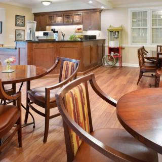 A cozy dining area with wooden tables and chairs, featuring a kitchen in the background.