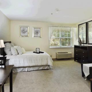 A spacious bedroom with elegant decor and furniture, featuring a bed, dresser, and large window.