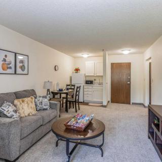 A cozy apartment living room with a sofa, coffee table, and a small dining area adjacent to a kitchenette.