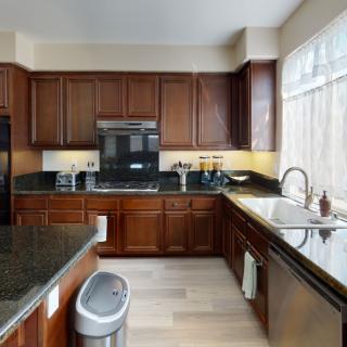 A modern kitchen with wooden cabinets and black countertops, featuring a sink, stove, oven, and ample natural light.