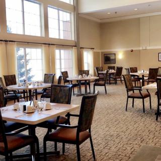 An empty dining room with neatly arranged tables and chairs, featuring large windows.