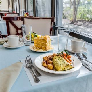 A breakfast table set with an omelette, potatoes, cake, and coffee near a window in a restaurant.
