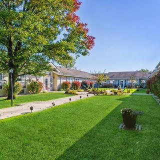 A beautifully maintained garden with a lush green lawn and a pathway leading to a charming building under a clear blue sky.