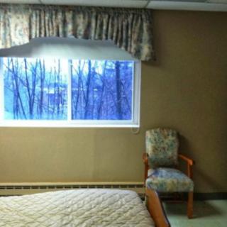 A bedroom interior with a window view, featuring a bed, chair, and curtains.
