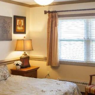 A cozy bedroom with a single bed, side table, lamp, and window with curtains.