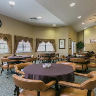 A neatly arranged dining room with round tables and chairs, decorated with curtains and lit by ceiling lights.