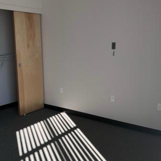 A minimalist empty room with sunlight casting shadows through a window, featuring a wooden sliding door.