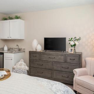 A modern bedroom interior featuring a dresser with a TV on top, a cozy pink chair, and decorative elements such as vases and flowers.