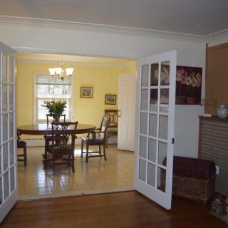 A cozy living room with French doors leading to a bright dining area with yellow walls and hardwood flooring.