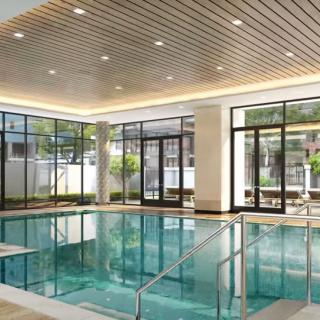 Modern indoor swimming pool with large windows and bright lighting.