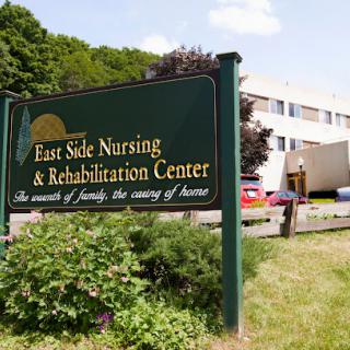 A view of the East Side Nursing & Rehabilitation Center, highlighting its welcoming sign amidst a green landscape.