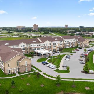 Aerial view of a large residential building complex with a parking lot and surrounding greenery.