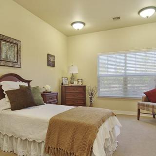 A cozy bedroom with traditional decor featuring a single bed, dresser, and window with blinds.