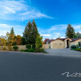 A suburban house with a driveway and surrounding trees under a blue sky with clouds.