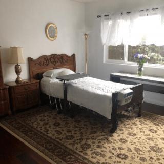 A cozy bedroom with a single bed and wooden furniture, featuring a large window and decorative items.