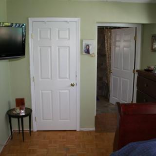A bedroom interior with a television mounted on a green wall, two white doors, and a small side table.