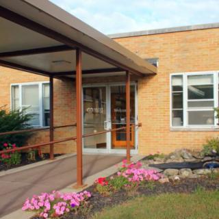 The entrance of a brick building with flowers and a canopy.