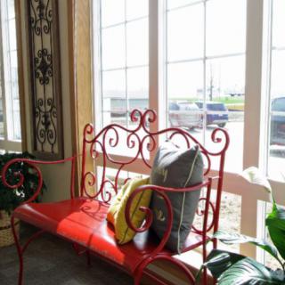 A decorative red bench with pillows by a sunlit window.