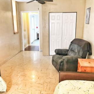 A cozy living room with an armchair, closet doors, and a ceiling fan, featuring tiled flooring and natural lighting.