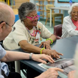Elderly individuals participate in a group activity at a community center, enjoying social interaction and shared reading.
