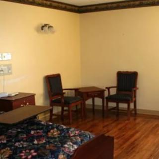 A simple room with two chairs, a small table, and a bed on a wooden floor.