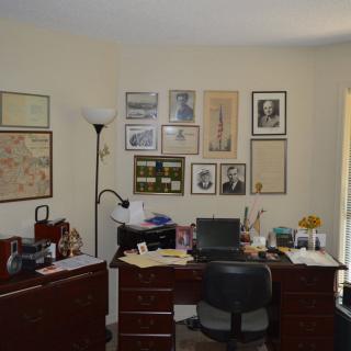 A home office with a desk, chair, and various photographs and documents on the wall.