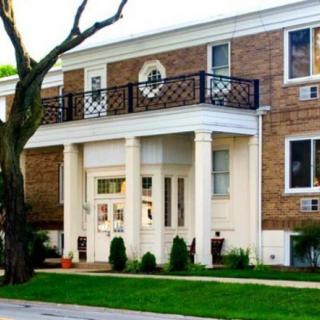A brick residential building with a prominent entrance featuring columns and a balcony.
