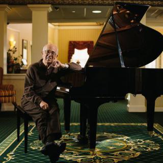 A man sits beside a grand piano in an elegant room.