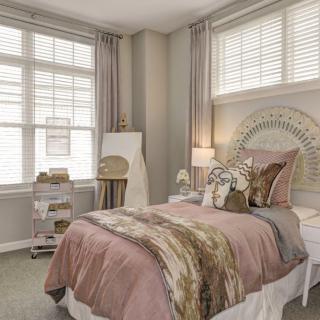 A cozy bedroom with pastel decor and large windows.