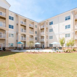 A residential apartment building with balconies and a grassy outdoor area featuring patio umbrellas.