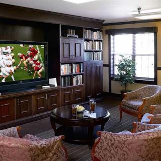 A cozy living room with a television showing a sports game, surrounded by bookshelves and comfortable seating.