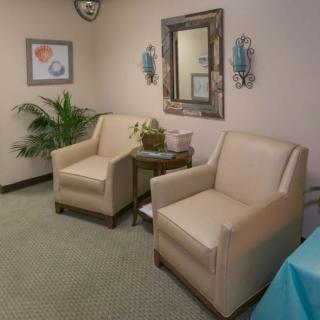 A cozy waiting room featuring two beige chairs, decorative wall art, and a potted plant.