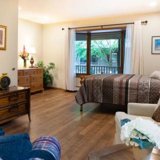 A cozy bedroom interior featuring wooden flooring, elegant furniture, and a view of greenery through the window.