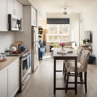 A modern apartment with an open kitchen and dining area, featuring natural light and wood flooring.