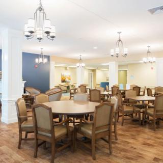 A spacious dining area with round tables, wooden chairs, and elegant chandeliers.