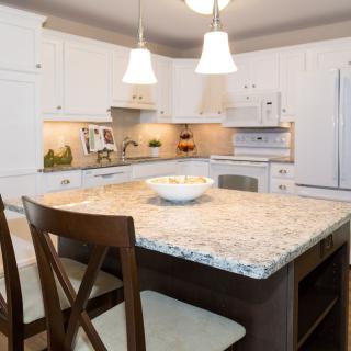 A modern kitchen featuring a central island with a granite countertop and pendant lighting.